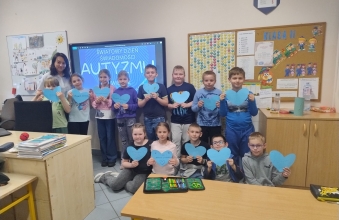 Uczniowie klasy drugiej stojacy z niebieskimi serduszkami podczas zajec zwiazanych z obchodami Swiatowego Dnia Swiadomosci Autyzmu