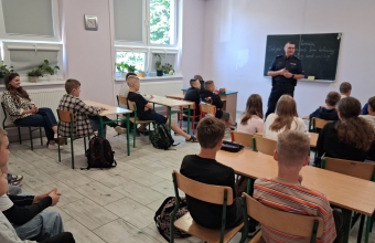 Klasa 4 i 5 siedzaca na krzeslach podczas spotkania z policjantem