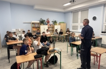 Klasa 6 i 7 siedzaca na krzeslach podczas spotkania z policjantem
